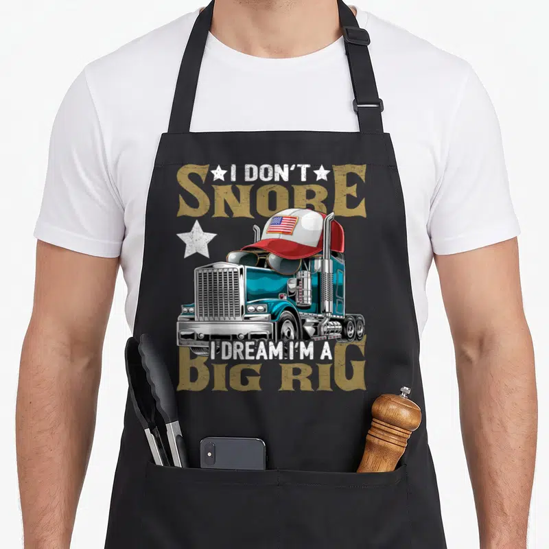 Snore rig apron - Cartoon semi-truck with cap sunglasses and text I don't snore I dream I'm a big rig — shown on a black cotton canvas apron against a white background