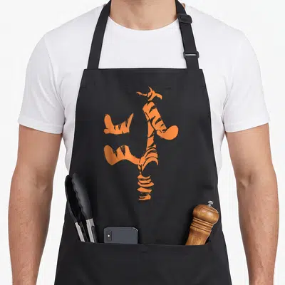 Sketch simple apron - Orange and black tiger sketch in a cartoon style with bouncy posture — shown on a black cotton canvas apron against a white background