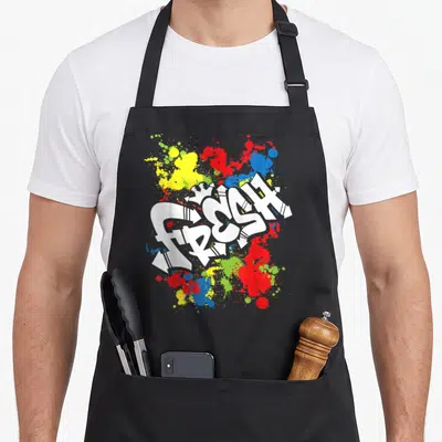 80s urban apron - White FRESH graffiti text over red yellow blue and green paint splatters — shown on a black cotton canvas apron against a white background