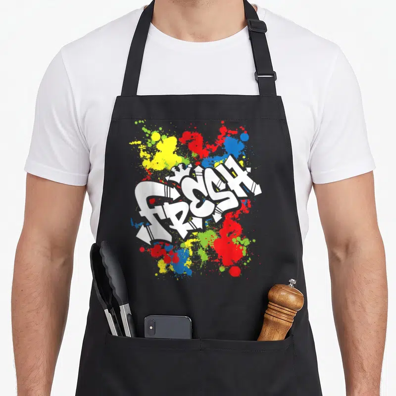 80s urban apron - White FRESH graffiti text over red yellow blue and green paint splatters — shown on a black cotton canvas apron against a white background