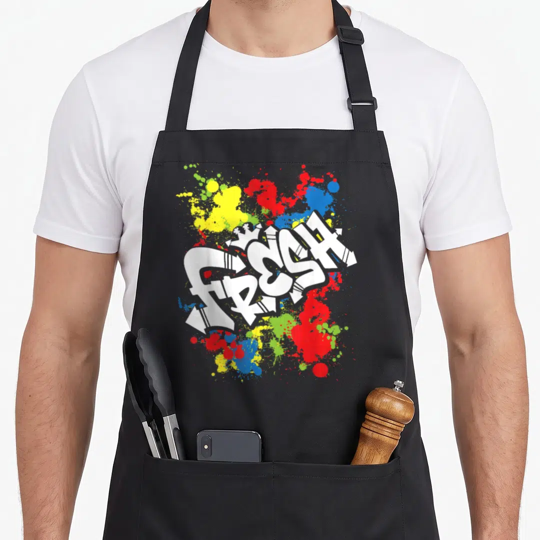 80s urban apron - White FRESH graffiti text over red yellow blue and green paint splatters — shown on a black cotton canvas apron against a white background