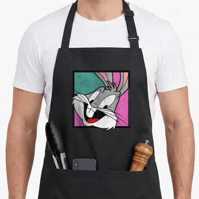 Box bunny apron - Bugs Bunny head over teal pink diagonal square, grey white fur, black border — shown on a black cotton canvas apron against a white background