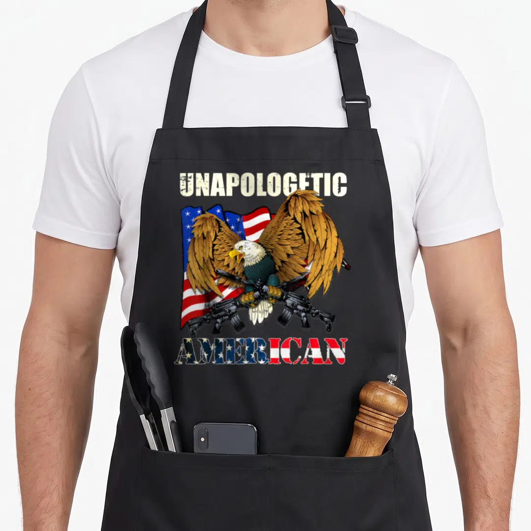Unapologetic eagle american flag apron - Bald eagle holding two rifles in front of a waving flag with unapologetic — shown on a black cotton canvas apron against a white background