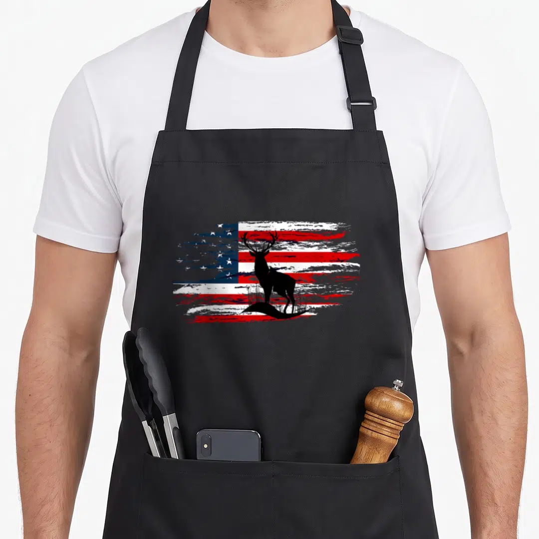 Patriotic grill hunter apron - Black deer silhouette standing before a distressed red white and blue flag design — shown on a black cotton canvas apron against a white background