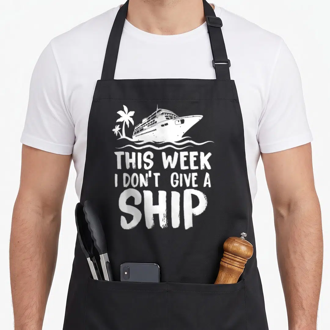 Week dont give apron - White distressed cruise ship and palm trees above stacked text THIS WEEK I DON'T GIVE A SHIP — shown on a black cotton canvas apron against a white background