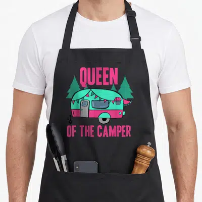 Queen happy camper apron - Pink teal cartoon camper trailer with pine trees and QUEEN OF THE CAMPER text — shown on a black cotton canvas apron against a white background