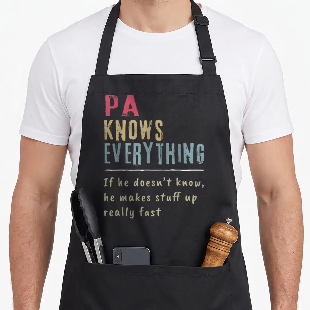 Vintage grandpa apron - Stacked PA KNOWS EVERYTHING text in red yellow blue and tan with white divider line — shown on a black cotton canvas apron against a white background