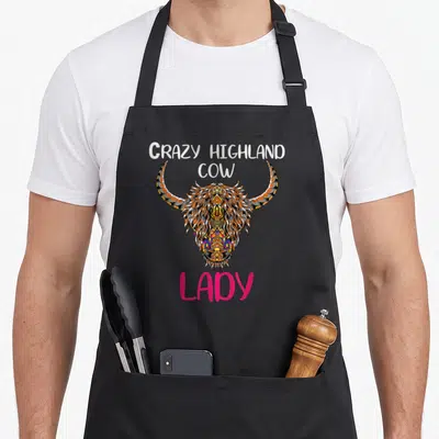 Funny highland cow print aprons - Line art highland cow head with orange blue pink details and stacked text Crazy — shown on a black cotton canvas apron against a white background