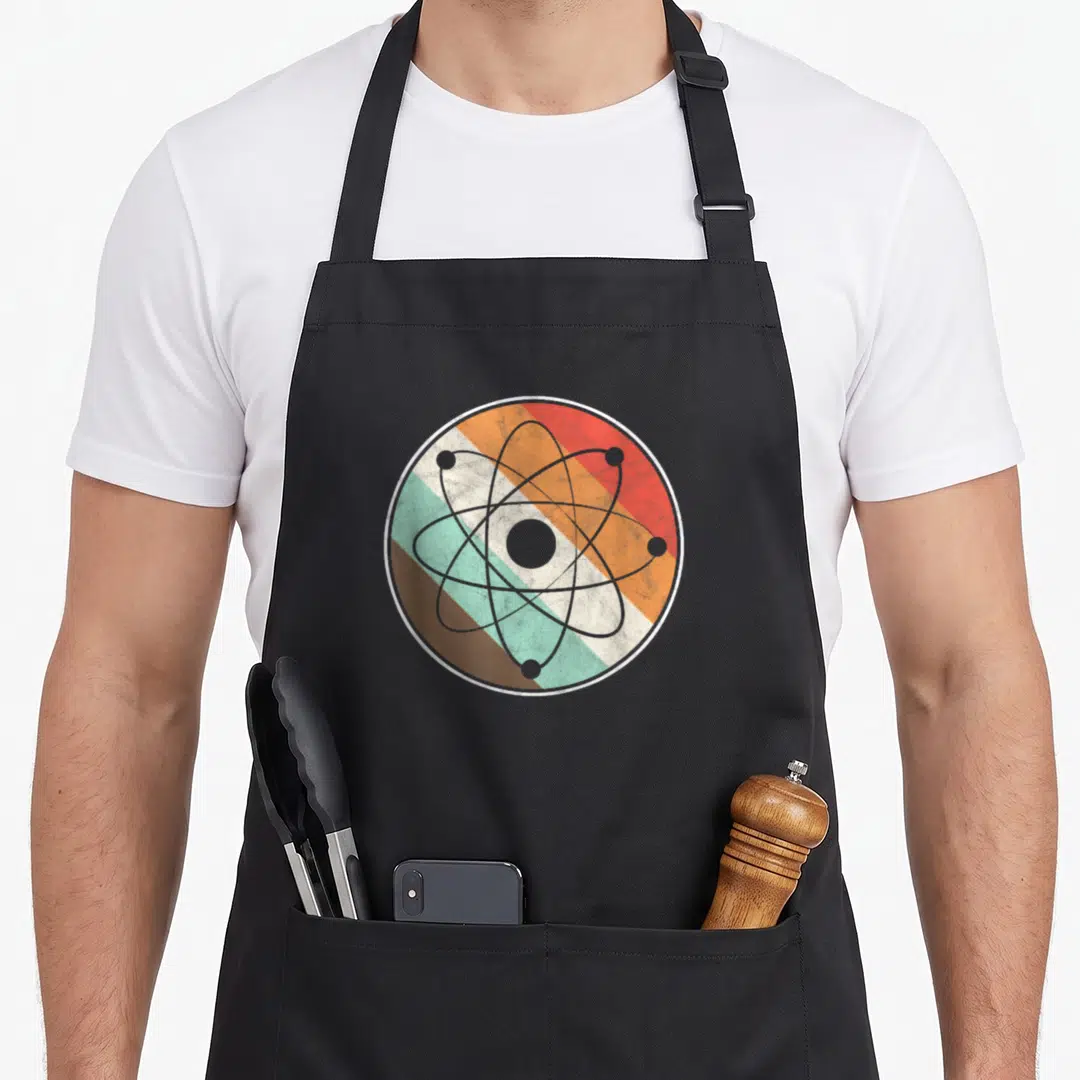 Physicist atom teacher apron - Grey atom symbol over retro red orange teal brown grey horizontal stripes — shown on a black cotton canvas apron against a white background