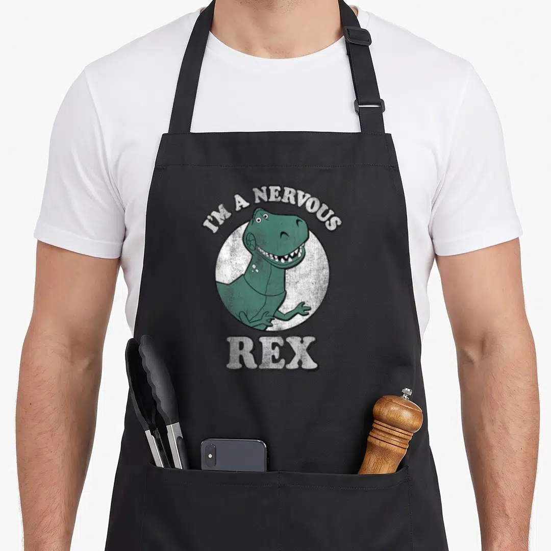 Nervous dinosaur apron - Green T-Rex inside white circle with I'M A NERVOUS REX text in distressed font — shown on a black cotton canvas apron against a white background