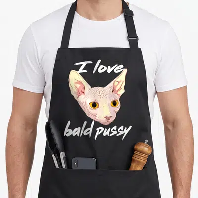 Bald dirty joke aprons - Realistic Sphynx cat head with I love bald pussy text in white and beige — shown on a black cotton canvas apron against a white background