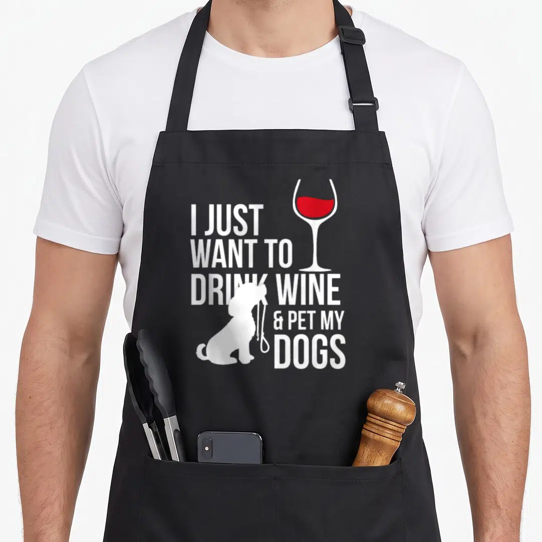 Drink wine dog apron - White stacked text I just want to drink wine and pet my dogs with red wine glass and dog — shown on a black cotton canvas apron against a white background