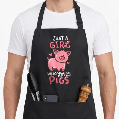 Pig farm aprons - Cartoon pink pig surrounded by three hearts with text Just A Girl Who Loves Pigs — shown on a black cotton canvas apron against a white background