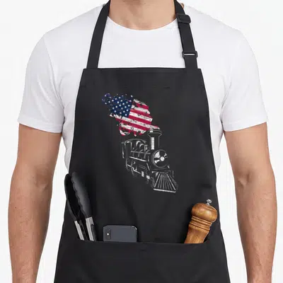 Locomotive patriotic apron - Distressed white steam locomotive with smoke filled with red, white, and blue USA flag — shown on a black cotton canvas apron against a white background