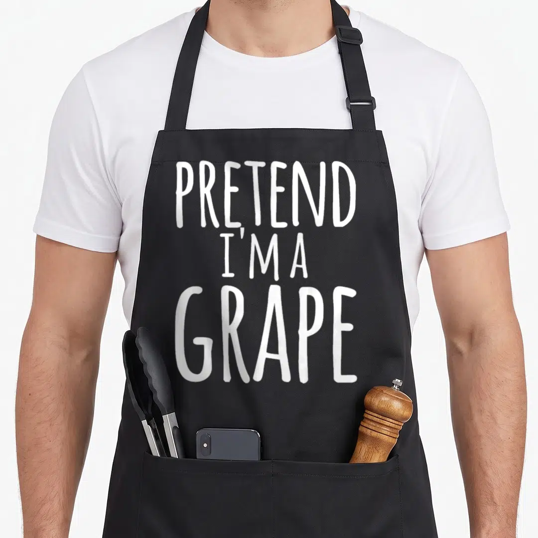 Lazy pretend halloween apron - White stacked text reading PRETEND I'M A GRAPE — shown on a black cotton canvas apron against a white background