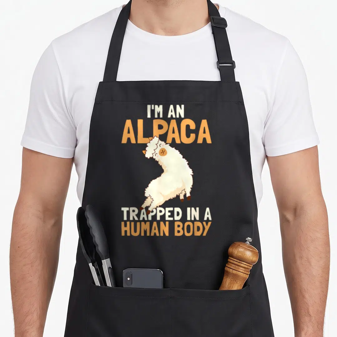 Human alpaca apron - Cartoon alpaca with text I'M AN ALPACA TRAPPED IN A HUMAN BODY in white and orange — shown on a black cotton canvas apron against a white background