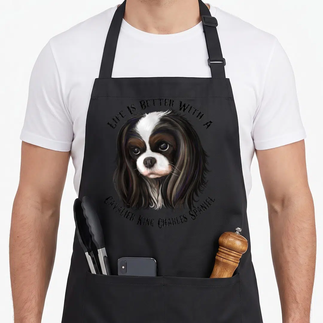 Cute cavalier king apron - Realistic tricolor spaniel head with arched text Life Is Better — shown on a black cotton canvas apron against a white background