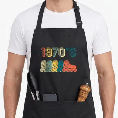 Roller skate 70s apron - 1970'S text above five overlapping quad skates in orange, yellow, green, beige, and teal — shown on a black cotton canvas apron against a white background
