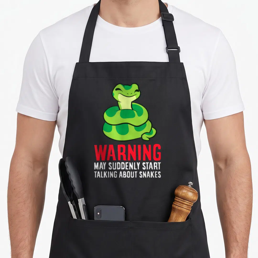 May talk about apron - Cartoon green coiled snake above red warning text and white slogan lines — shown on a black cotton canvas apron against a white background