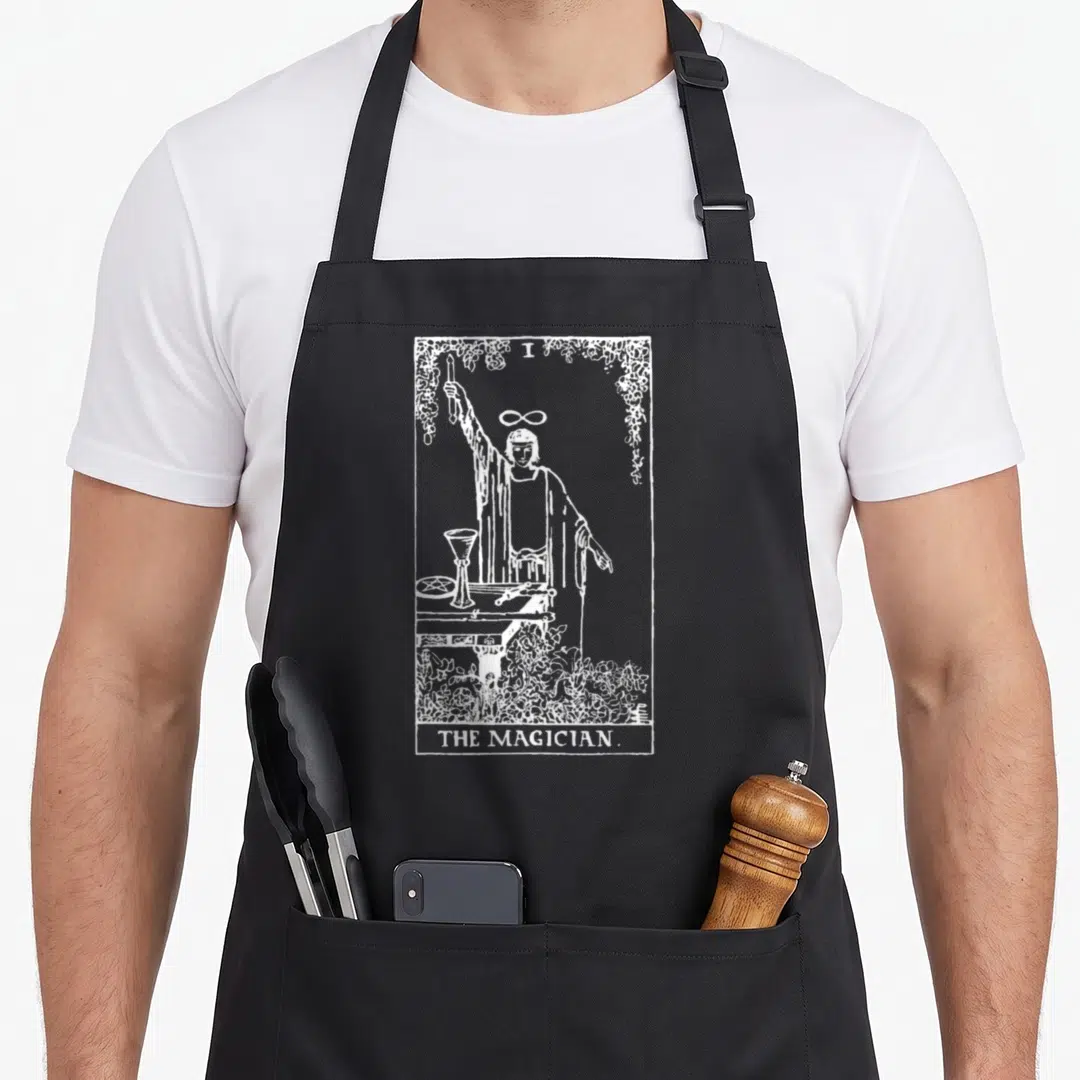 Magician traditional apron - White line art of The Magician tarot figure with floral border and text — shown on a black cotton canvas apron against a white background