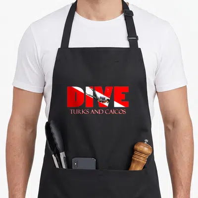 Turk snorkeling apron - DIVE TURKS AND CAICOS text with red white stripes and swimming scuba diver cartoon — shown on a black cotton canvas apron against a white background