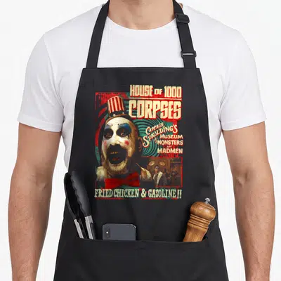 Captain zombie apron - Distressed clown head with House of 1000 Corpses text and Fried Chicken Gasoline slogan — shown on a black cotton canvas apron against a white background