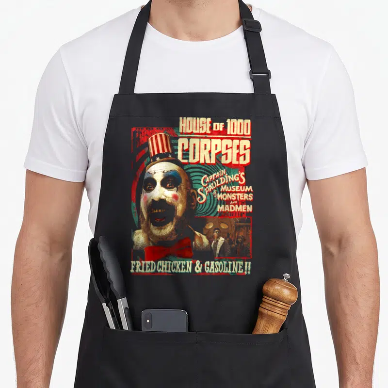 Captain zombie apron - Distressed clown head with House of 1000 Corpses text and Fried Chicken Gasoline slogan — shown on a black cotton canvas apron against a white background