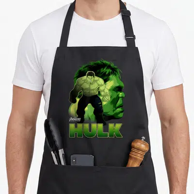 Profile infinity apron - Hulk full body standing before a large green profile face with Avengers Infinity War logo — shown on a black cotton canvas apron against a white background