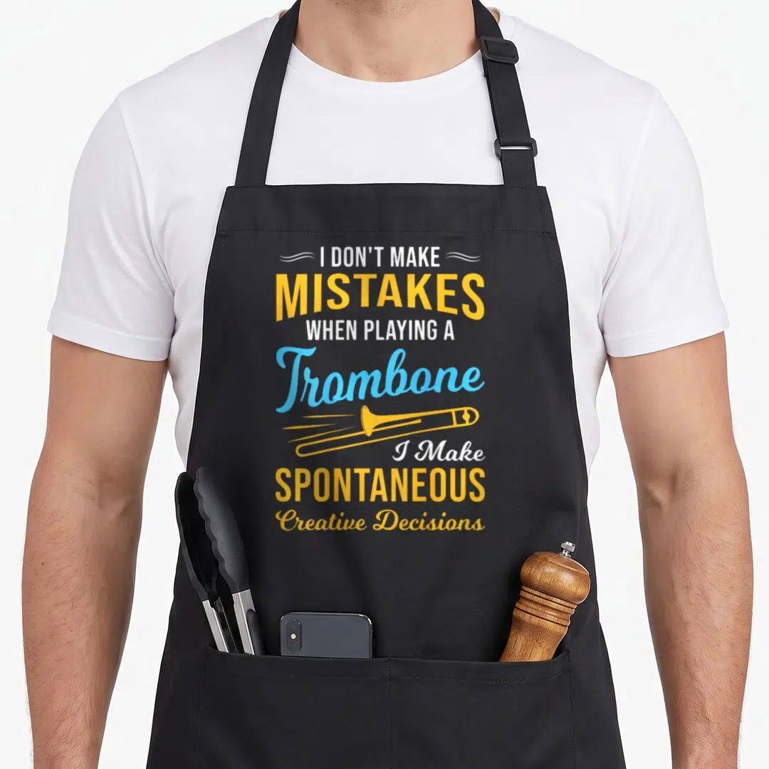 Playing trombone quotes apron - Yellow trombone illustration between white and blue text reading I don't make mistakes — shown on a black cotton canvas apron against a white background