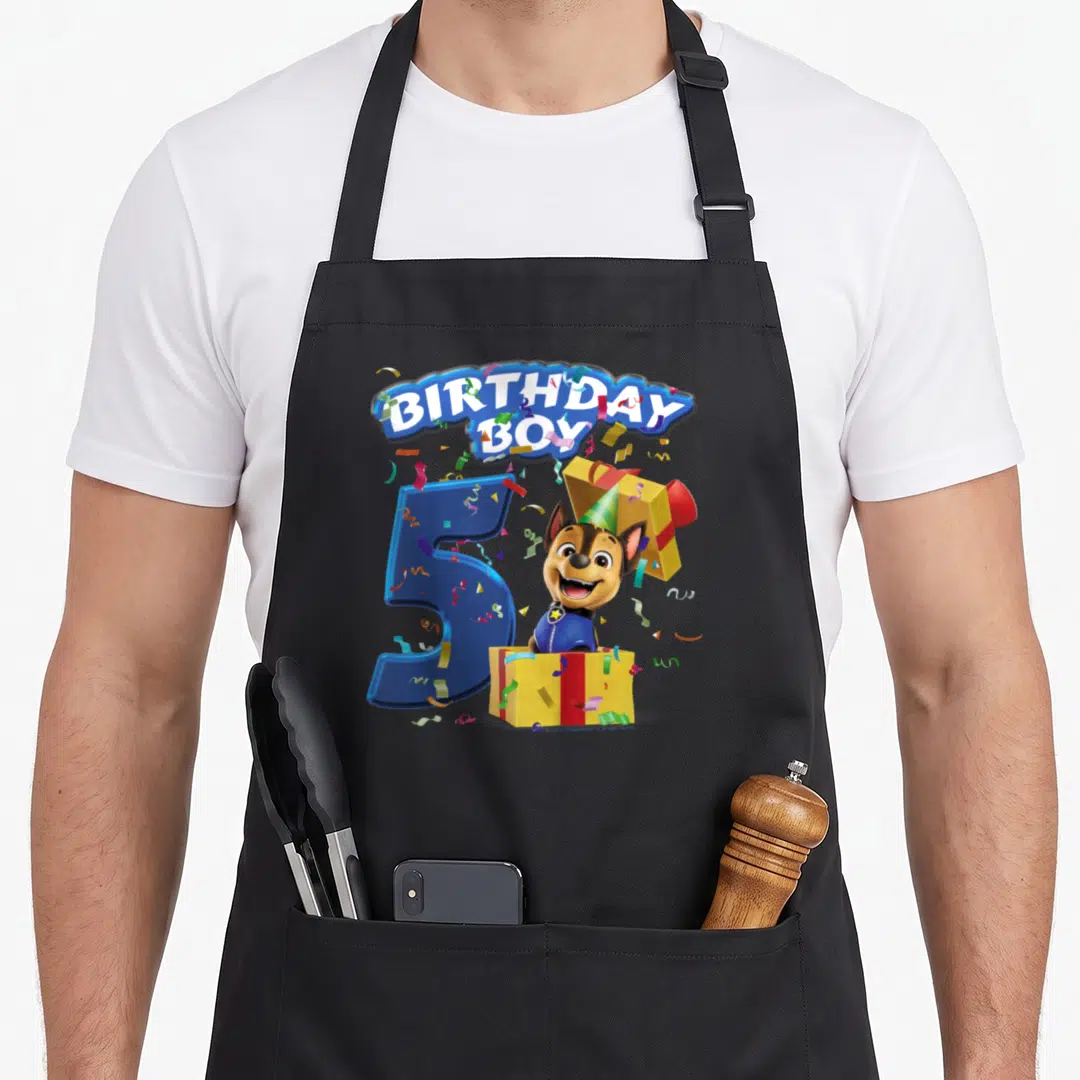 Vintage chase birthday apron - Cartoon dog in party hat emerging from gift box next to blue number 5 under arched text — shown on a black cotton canvas apron against a white background