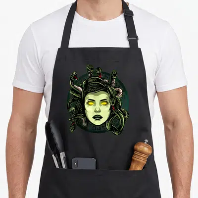 Monster greek aprons - Cartoon Medusa face with green snakes and yellow eyes on a dark green circular emblem — shown on a black cotton canvas apron against a white background