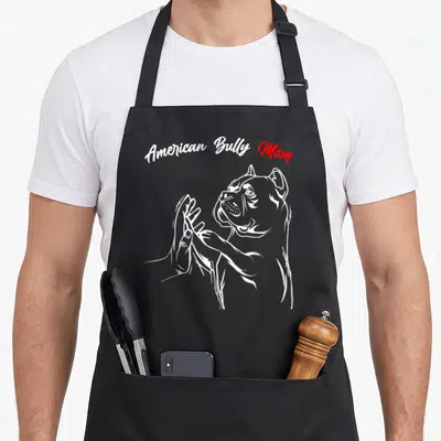 Bully personalized dog apron - Arched American Bully Mom text above white line art of dog paw shaking human hand — shown on a black cotton canvas apron against a white background