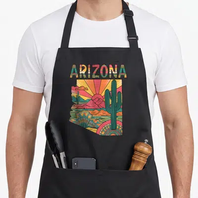 Arizona flag cactus apron - Retro Arizona state map print with cacti, mountains, and sun in orange, green, pink — shown on a black cotton canvas apron against a white background