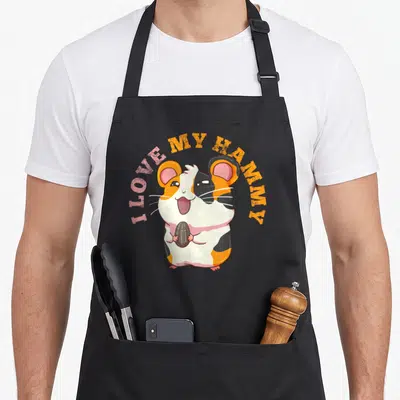 Funny best hamster apron - Cartoon hamster holding a seed with I LOVE MY HAMMY text arched above — shown on a black cotton canvas apron against a white background