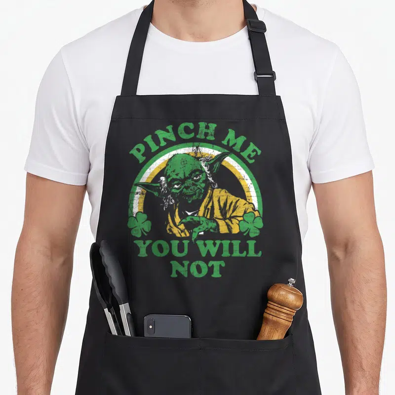 Pinch st patrick day aprons - Distressed Yoda portrait in green and yellow with PINCH ME YOU WILL NOT text and two — shown on a black cotton canvas apron against a white background