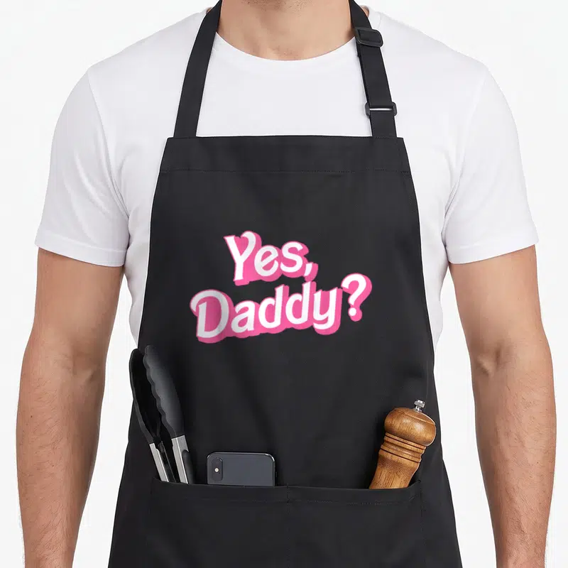 Ddlg daddy apron - Yes Daddy text in white with pink outline stacked in two lines — shown on a black cotton canvas apron against a white background
