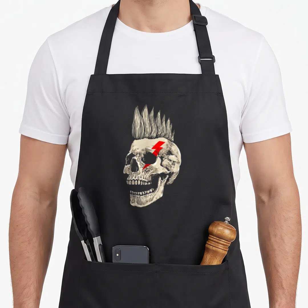 Skull punk rock apron - Beige skull with mohawk, red lightning bolt, and PUNKS NOT DEAD text — shown on a black cotton canvas apron against a white background