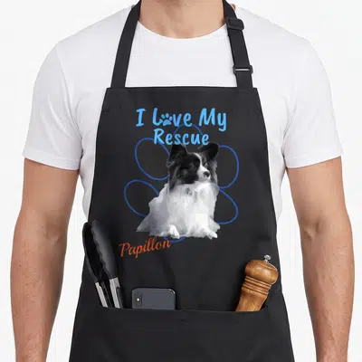 Adopted dog apron - I Love My Rescue Papillon photo design with blue circles and orange script text — shown on a black cotton canvas apron against a white background