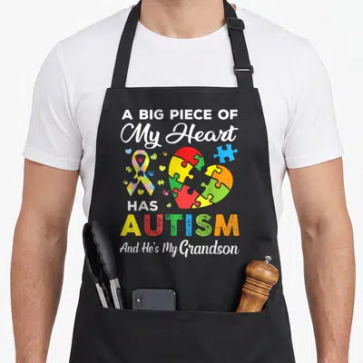 Autism grandson apron - Colorful puzzle heart and ribbon with text A Big Piece Of My Heart Has Autism And He's My — shown on a black cotton canvas apron against a white background