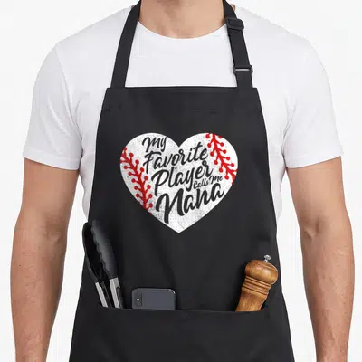 Player call grandma apron - White heart with red stitching and grey text My Favorite Player Calls Me Nana — shown on a black cotton canvas apron against a white background
