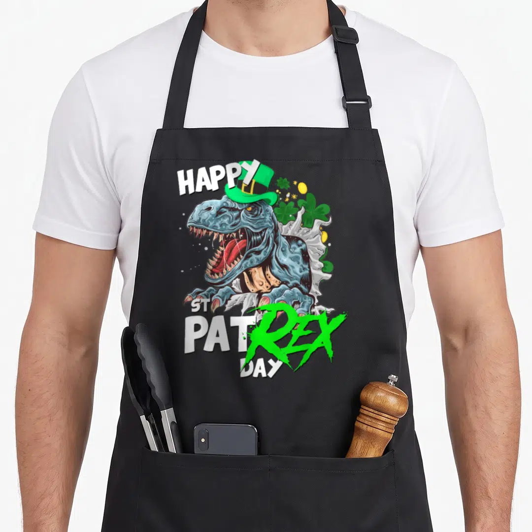 Rex st patrick day aprons - T-Rex in green hat with shamrocks and HAPPY ST PAT REX DAY text — shown on a black cotton canvas apron against a white background