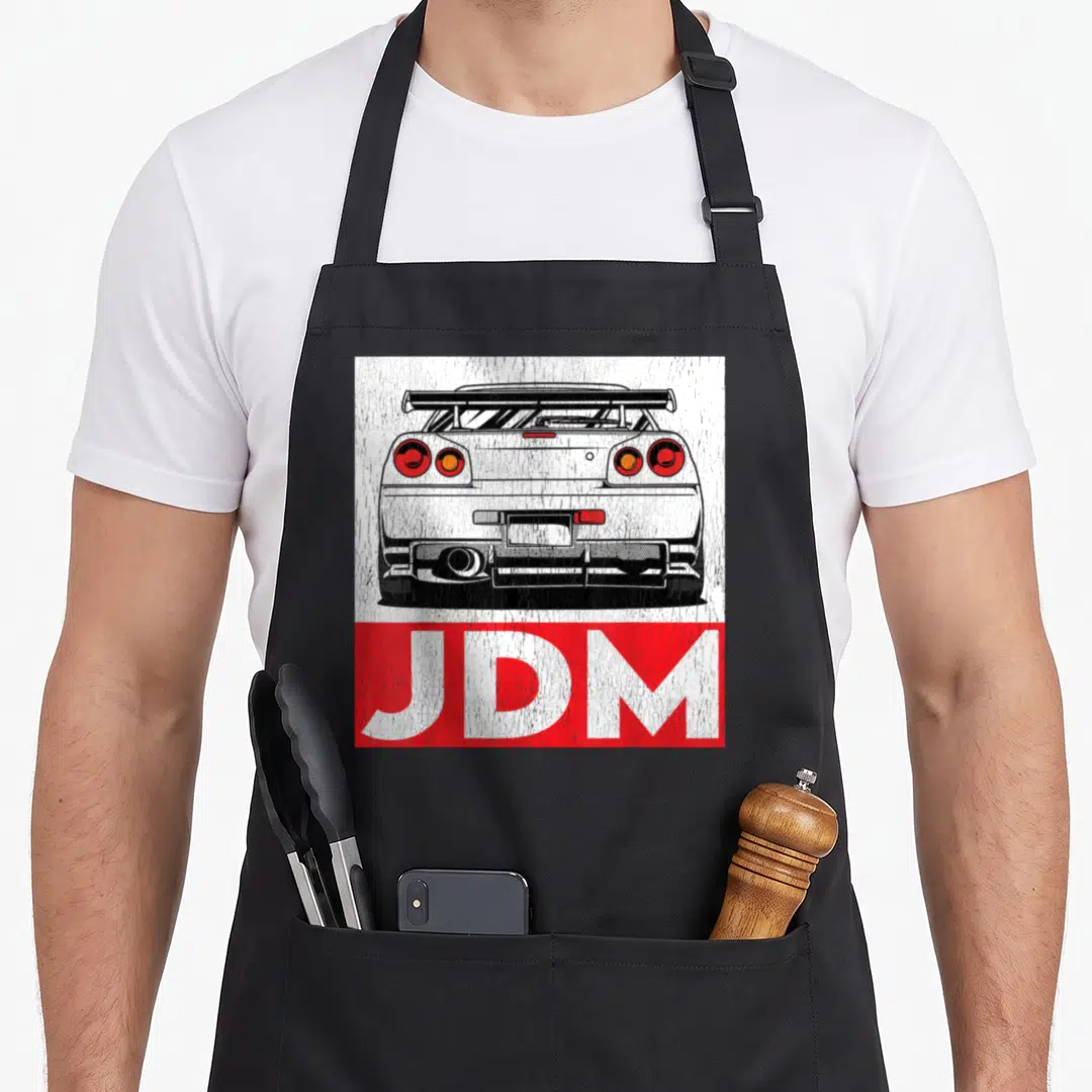 Turbo design imports vintage apron - Distressed rear car drawing above red JDM text block in white red black — shown on a black cotton canvas apron against a white background