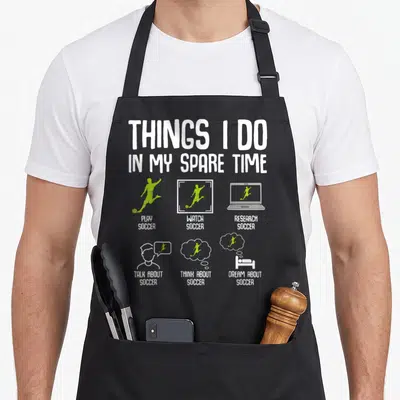 Spare soccer player accessories apron - Text listing playing watching researching talking thinking and dreaming about — shown on a black cotton canvas apron against a white background