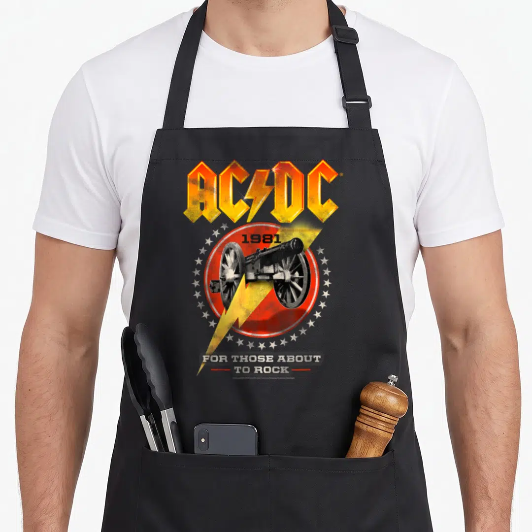 Those ac dc apron - AC/DC logo, 1981 cannon in red circle, yellow lightning bolt, white stars, and stacked text — shown on a black cotton canvas apron against a white background