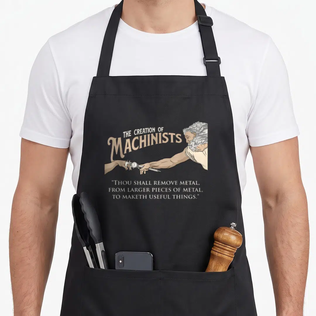 Milling machinist apron - Bearded figure handing a dial caliper to another hand under beige arching text and white — shown on a black cotton canvas apron against a white background