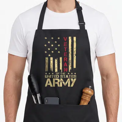 Patriotic american flag apron - Distressed tan stars and stripes with vertical red VETERAN text and stacked Army — shown on a black cotton canvas apron against a white background