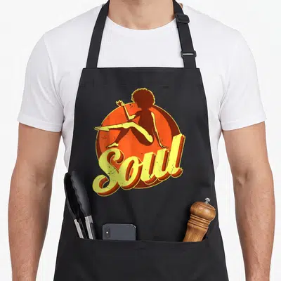 Music 70s apron - Retro woman silhouette sitting before orange circle with yellow Soul script text — shown on a black cotton canvas apron against a white background