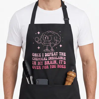 Anxiety psychology apron - Pink angry cartoon brain with arms legs and four line text about chemical imbalance sarcasm — shown on a black cotton canvas apron against a white background