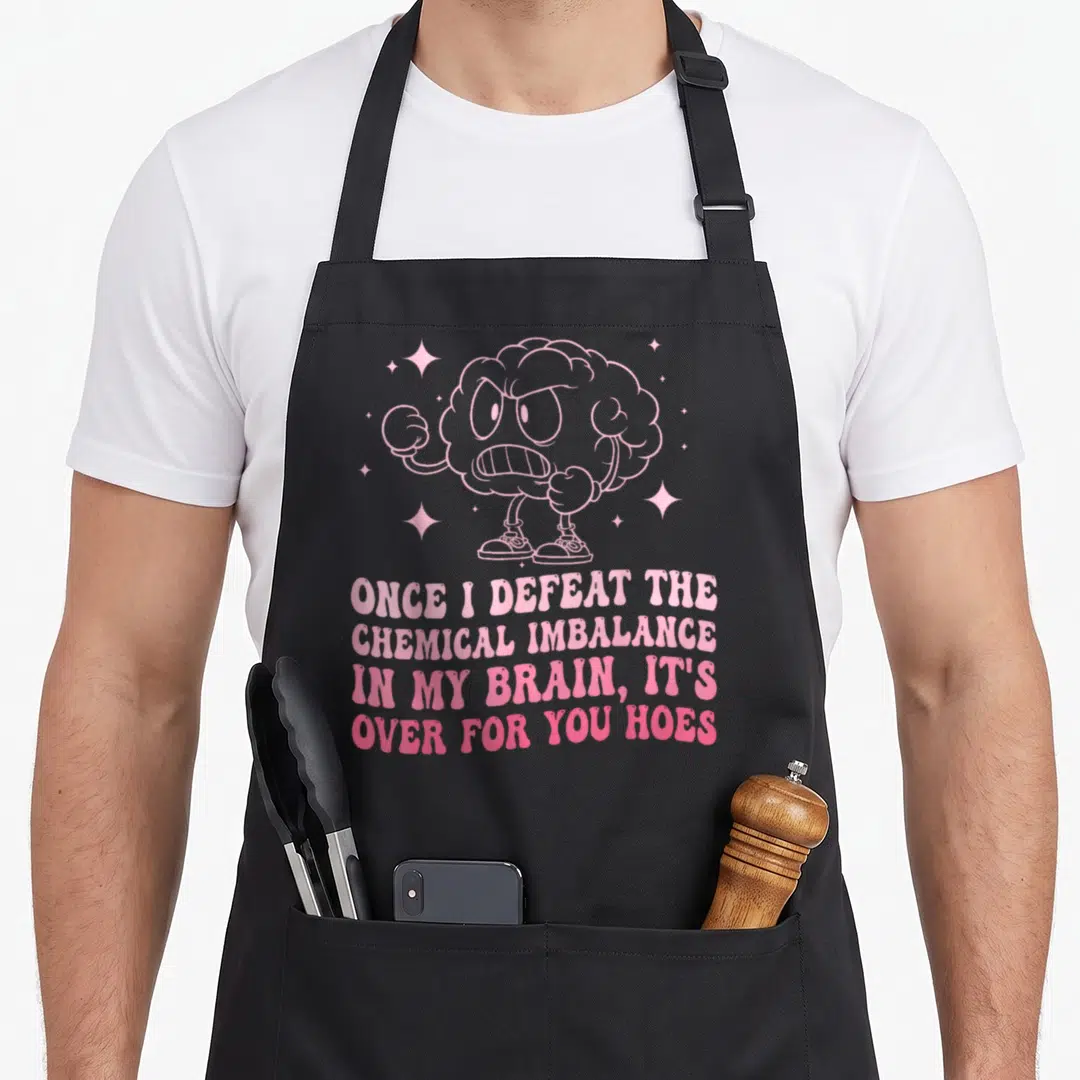 Anxiety psychology apron - Pink angry cartoon brain with arms legs and four line text about chemical imbalance sarcasm — shown on a black cotton canvas apron against a white background