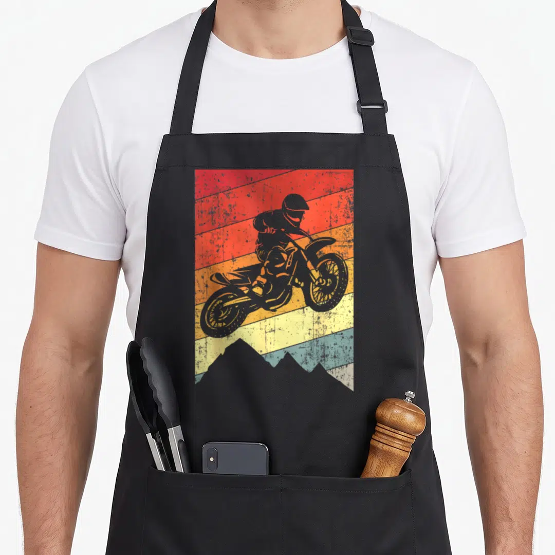 Dirtbike bike apron - Grey motocross rider silhouette over red orange yellow teal grey horizontal stripes and mountain — shown on a black cotton canvas apron against a white background
